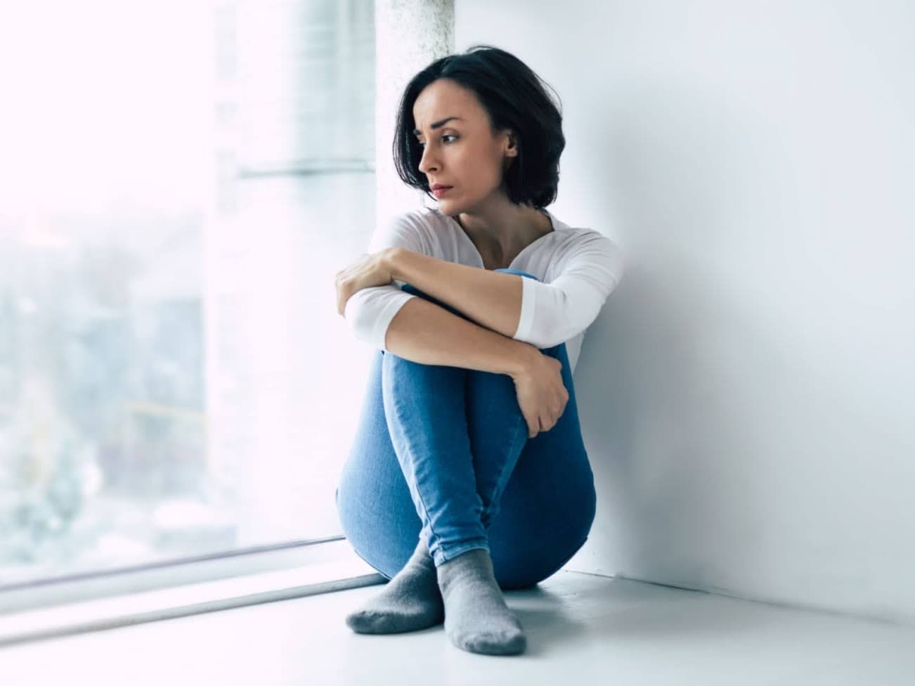A woman sitting on the floor near a window